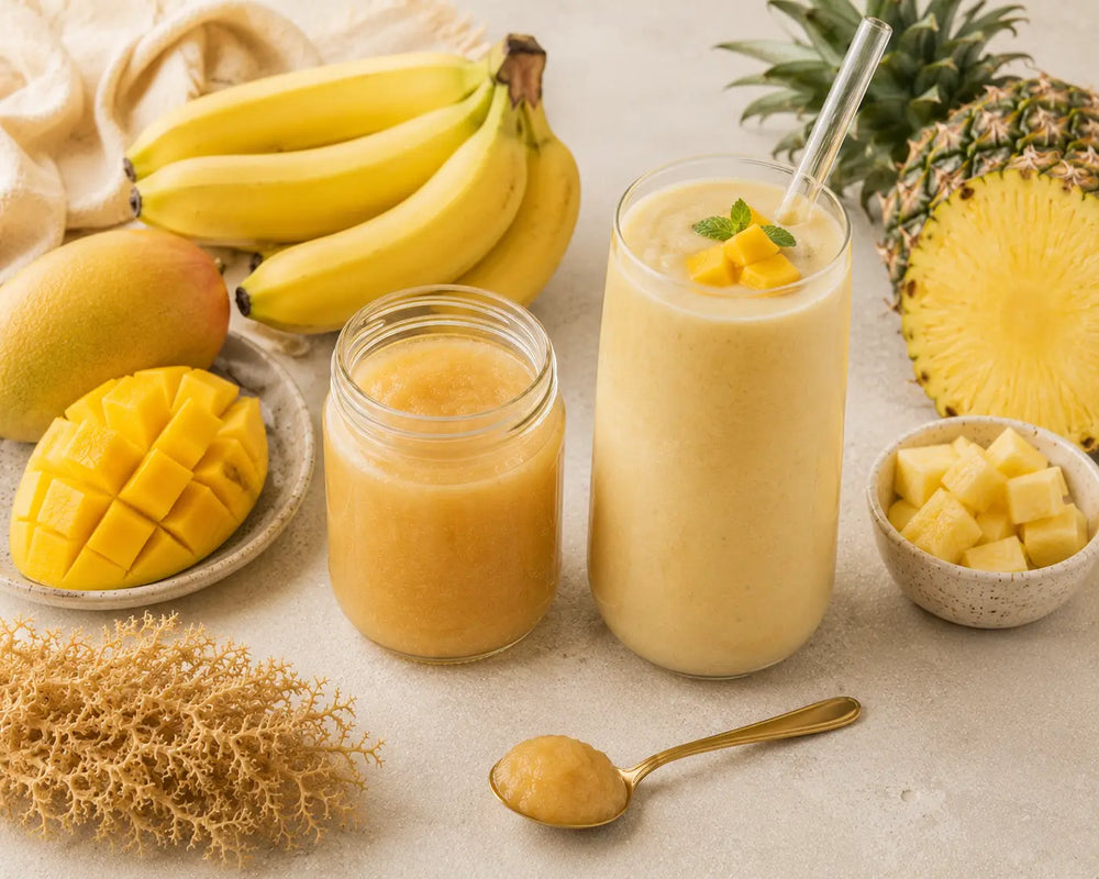 Jar of golden sea moss gel beside a fruit smoothie with banana, mango and pineapple.