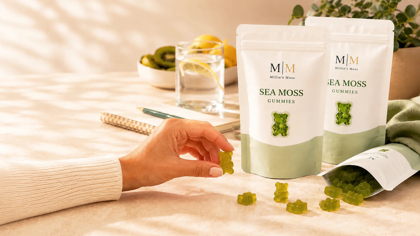 Millie’s Moss sea moss gummies pouches on a warm kitchen counter with loose gummies, fruit, and a glass of lemon water.