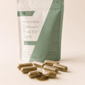 Close-up of Bladderwrack & Burdock Root Capsules with herbal powder visible inside the capsules and the pouch softly blurred in the background.