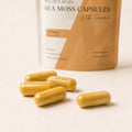 Close-up of Millie’s Moss Sea Moss with Turmeric Capsules showing golden turmeric-toned capsules on a warm off-white surface