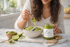 Woman adding matcha sea moss gel to smoothie bowl with kiwi blueberries and superfood toppings